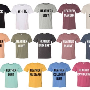 May include: A collection of 18 t-shirts in various colors, including black, white, heather grey, heather maroon, soft cream, heather peach, heather olive, heather dark grey, heather mauve, heather navy, heather mint, heather mustard, heather columbia blue, and heather raspberry. Each shirt has a different color and a text label indicating the color.