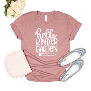 May include: A mauve t-shirt with the text "hello kindergarten" in white lettering and a white pencil graphic.