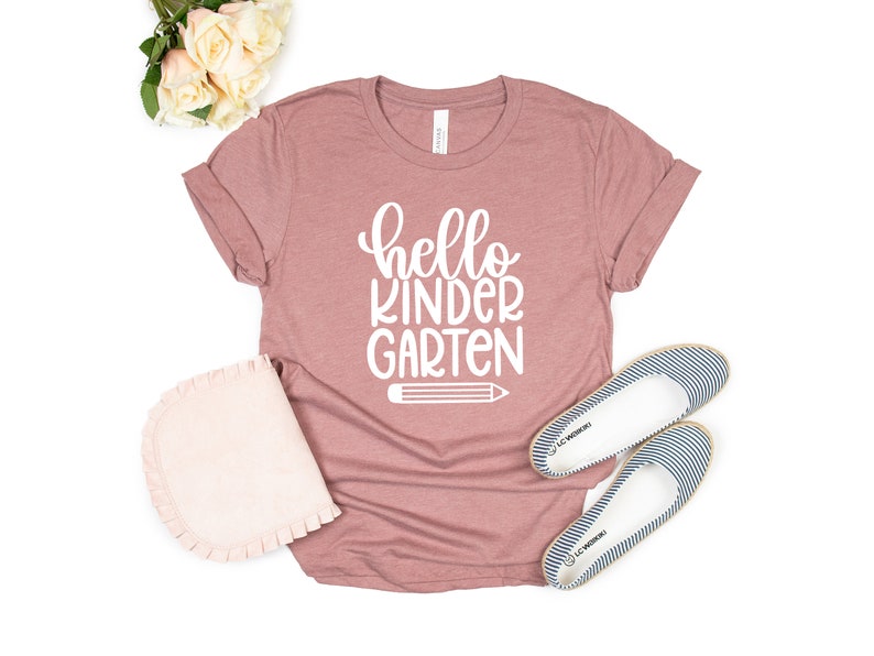 May include: A mauve t-shirt with the text "hello kindergarten" in white lettering and a white pencil graphic.