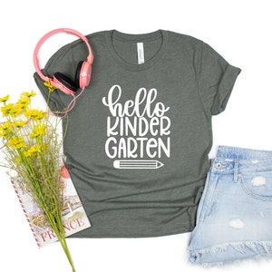 May include: A dark green t-shirt with the text "hello kindergarten" in white lettering and a white pencil graphic.