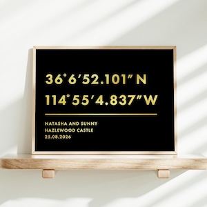 May include: A framed black print with gold text and a wooden frame. The text includes coordinates, names, a location, and a date. The coordinates read 36°6'52.101"N 114°55'4.837"W. The names Natasha and Sunny are listed, along with Hazlewood Castle and the date 25.08.2026.