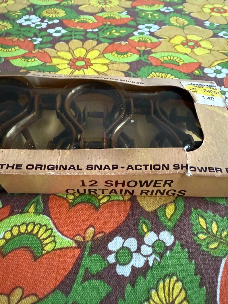 May include: A package of 12 brown snap-action shower curtain rings. The cardboard box has the text "THE ORIGINAL SNAP-ACTION SHOWER" and "12 SHOWER CURTAIN RINGS". The background is a floral pattern with orange, yellow, and green flowers.