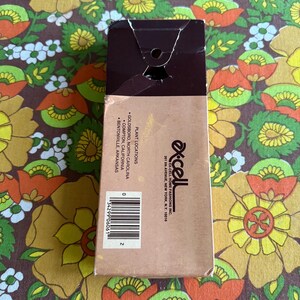 May include: A brown cardboard box with a torn top, featuring the brand name "Ex-Cell" and a barcode. The box lists plant locations in Goldsboro, Compton, and Bentonville. The background is a floral pattern.