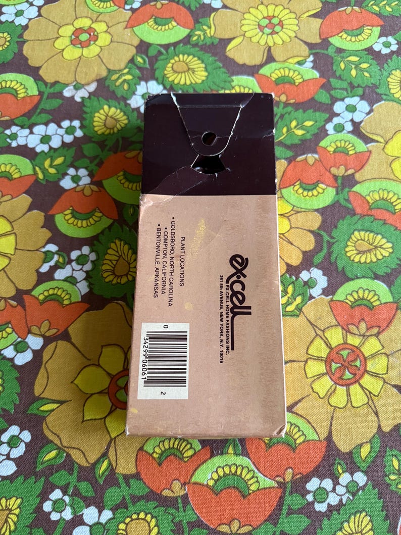 May include: A brown cardboard box with a torn top, featuring the brand name "Ex-Cell" and a barcode. The box lists plant locations in Goldsboro, Compton, and Bentonville. The background is a floral pattern.