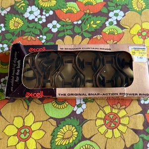 May include: A vintage box of Excell shower curtain rings. The box is brown and black with the text "an added touch of elegance for the bath" and "THE ORIGINAL SNAP-ACTION SHOWER RING". The box contains bronze-colored shower curtain rings.