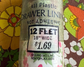 May include: A roll of clear plastic drawer lining with a floral pattern of pink flowers and green leaves on a white background. The label reads "All Plastic Drawer Lining, Not Adhesive, 12 Feet, 18" Wide."