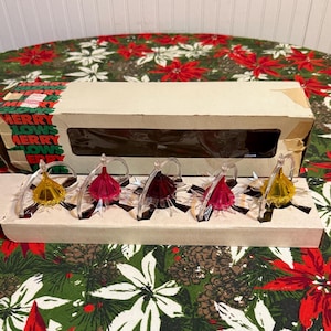 May include: A vintage Christmas light set with five decorative lights in a cardboard box. The lights have clear plastic bases and are topped with yellow, pink, and red colored ornaments. The box has the words "MERRY GLOWS" printed on it.