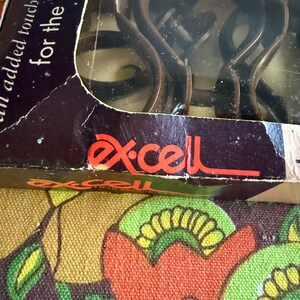 May include: A package of Ex-cell brand shower curtain hooks. The box is dark with the words "an added touch of elegance for the bath". The hooks are dark brown and visible through the clear plastic.