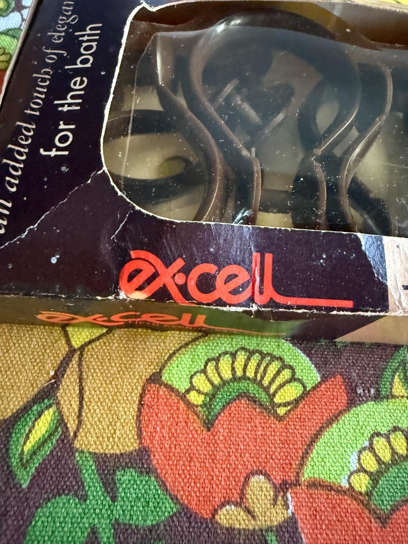 May include: A package of Ex-cell brand shower curtain hooks. The box is dark with the words "an added touch of elegance for the bath". The hooks are dark brown and visible through the clear plastic.