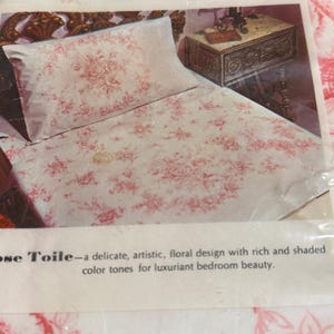 May include: A package of Lady Pepperell Rose Toile bedding. The bedding features a white background with a repeating pattern of pink roses. The packaging includes text that reads "Amazing Performance" and "Needs No Ironing".
