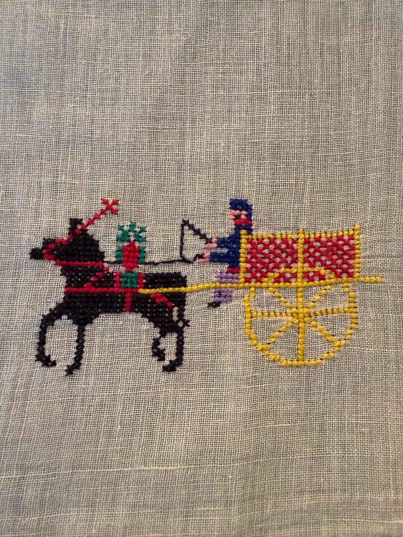 May include: Cross-stitch embroidery of a horse-drawn cart with a driver. The horse is black with red accents, pulling a yellow and red cart. The driver wears blue and purple. The background is a light beige fabric.