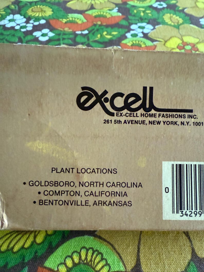 May include: A close-up of a cardboard box with the "Ex-Cell Home Fashions Inc." logo and address. The text "Plant Locations" is visible, listing Goldsboro, North Carolina; Compton, California; and Bentonville, Arkansas.