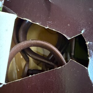 May include: A partially visible brown cardboard box with a torn edge, revealing a glimpse of a brown object inside. The object appears to be a coiled, circular structure, possibly a part of a larger item.