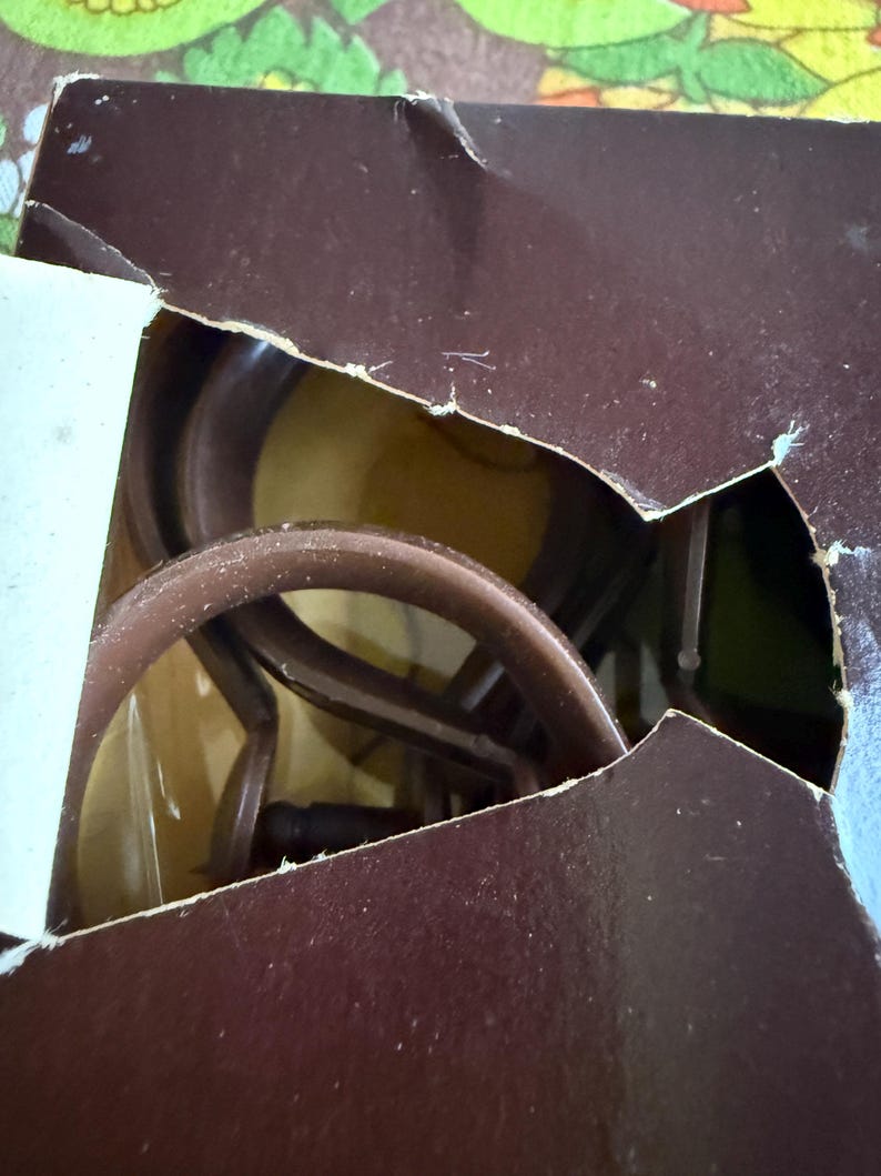 May include: A partially visible brown cardboard box with a torn edge, revealing a glimpse of a brown object inside. The object appears to be a coiled, circular structure, possibly a part of a larger item.