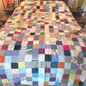 May include: A patchwork quilt with a vibrant mix of colors and patterns, including squares of red, blue, yellow, and green. The quilt is spread over a bed, showcasing its handmade quality and vintage aesthetic.