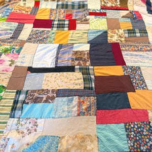 May include: A patchwork quilt featuring a variety of fabrics in a vibrant array of colors and patterns. The quilt is composed of numerous rectangular and square patches, creating a textured and visually appealing design. The quilt's dimensions are not visible.