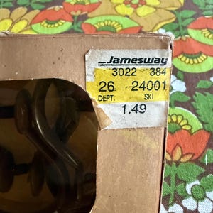 May include: A partially visible cardboard box with a yellow price tag from Jamesway. The tag displays numbers and the word "SKI". The background features a floral pattern in shades of brown, orange, yellow, and green.