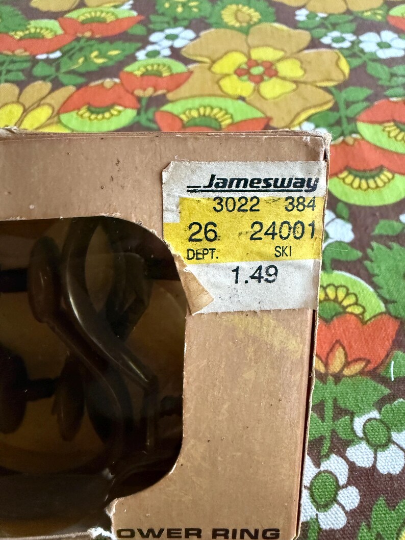 May include: A partially visible cardboard box with a yellow price tag from Jamesway. The tag displays numbers and the word "SKI". The background features a floral pattern in shades of brown, orange, yellow, and green.