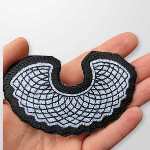 May include: A black and white embroidered iron-on patch in the shape of a  RBG collar.