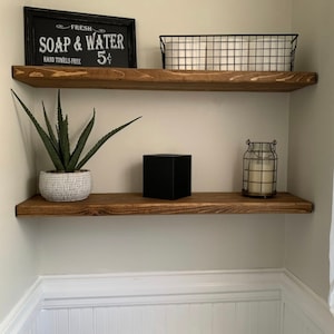 May include: Two wooden shelves with a black sign that reads "FRESH SOAP & WATER 5¢ HAND TOWELS FREE", a black wire basket with white towels, a black square box, a white planter with a green succulent plant, and a clear glass candle holder with a white candle.