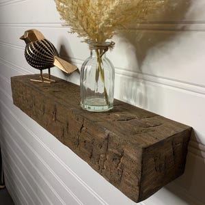 May include: A rustic wooden shelf with a distressed finish, featuring a decorative bird figurine and a glass vase with dried pampas grass.
