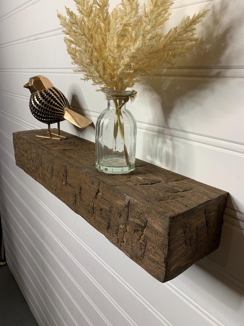 May include: A rustic wooden shelf with a distressed finish, featuring a decorative bird figurine and a glass vase with dried pampas grass.
