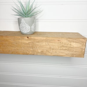 May include: A light wood shelf with a small potted plant on top. The plant has light green leaves and is in a grey pot with a white design.