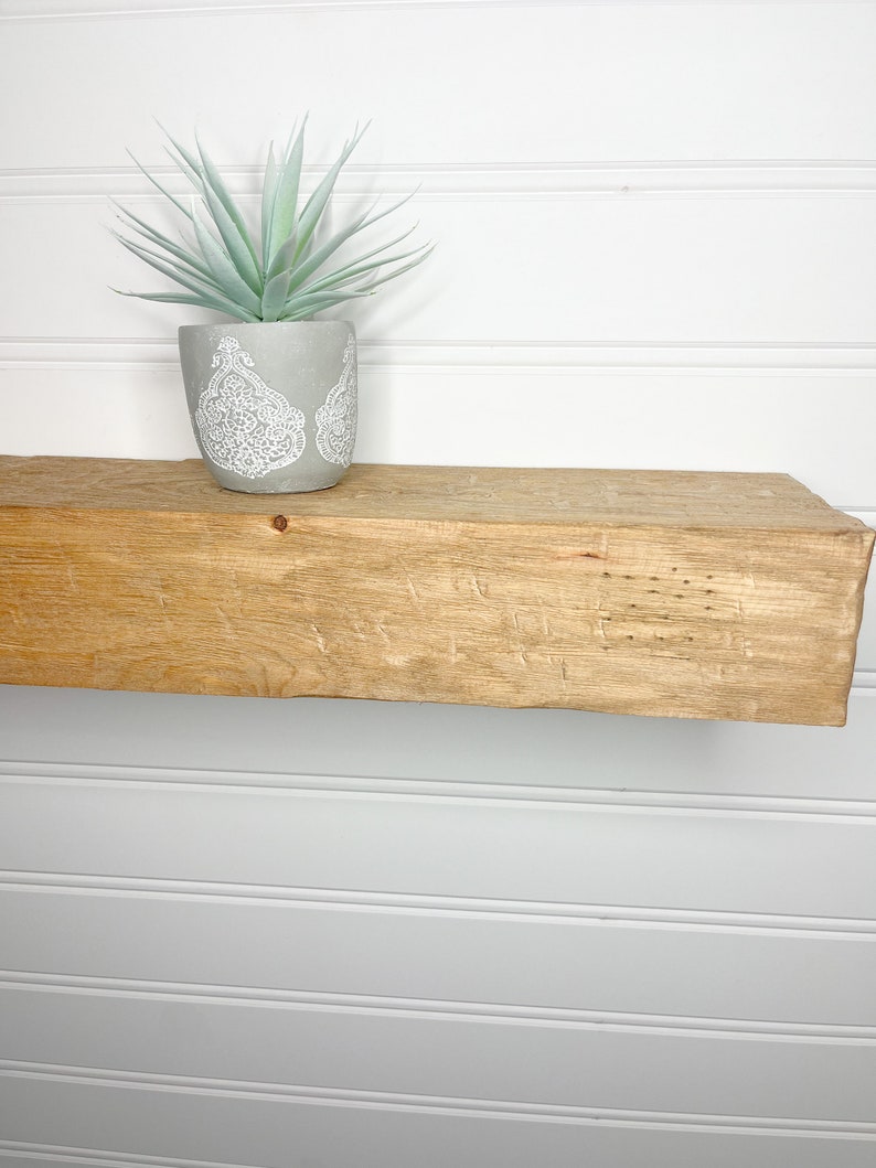 May include: A light wood shelf with a small potted plant on top. The plant has light green leaves and is in a grey pot with a white design.