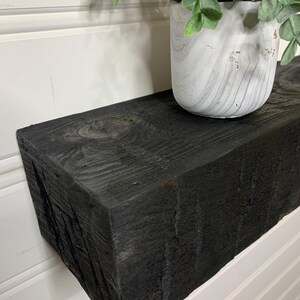 May include: Black wooden shelf with a white planter and green plant on top. The shelf is made of reclaimed wood and has a rustic look.