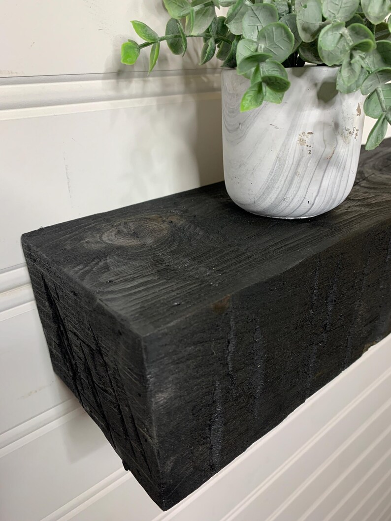 May include: Black wooden shelf with a white planter and green plant on top. The shelf is made of reclaimed wood and has a rustic look.