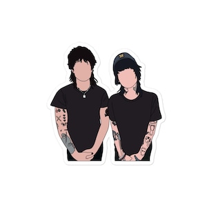 May include: Two people with black hair and black shirts. The person on the left has tattoos on their arms. The person on the right is wearing a black hat with a yellow logo.