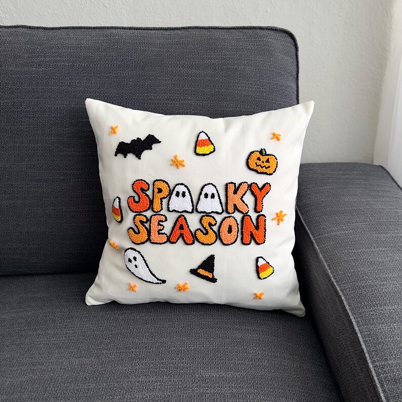 May include: White pillow with the text "Spooky Season" in orange and black letters. The pillow is decorated with embroidered ghosts, bats, candy corn, and a pumpkin.