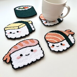 May include: Five handmade sushi-shaped coasters with smiling faces. The coasters are made of white yarn with different colored toppings, including green, yellow, orange, and pink. The coasters are perfect for adding a touch of whimsy to your home decor.