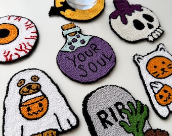 May include: Set of eight Halloween-themed coasters featuring various designs, including a ghost, a skull, an eye, a potion bottle, a cat, and a tombstone. The coasters are made of white yarn and feature colourful details.