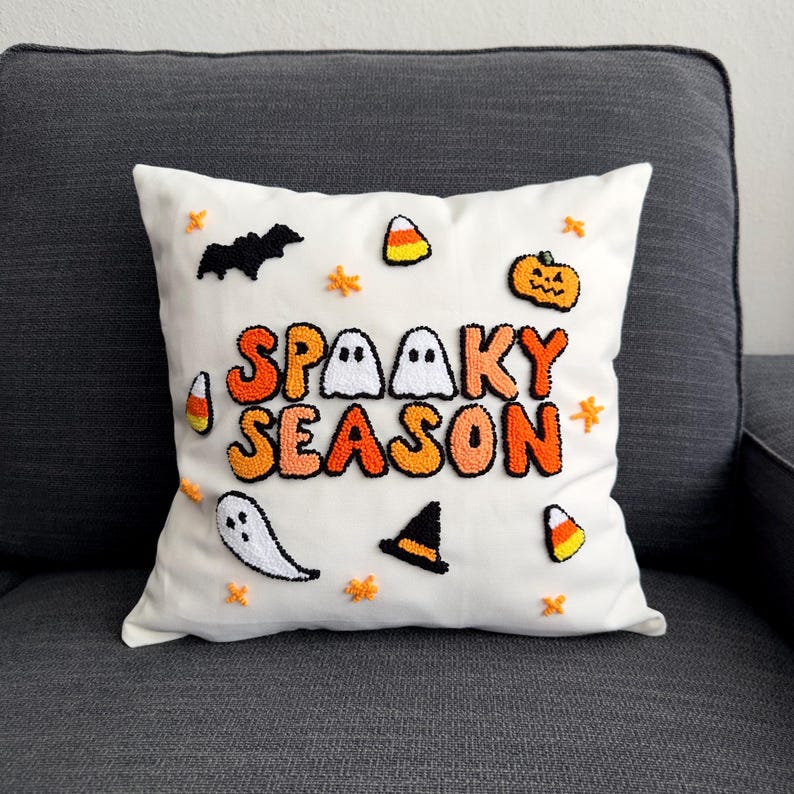 May include: White pillow with the text "Spooky Season" in orange, black, and white letters. The pillow is decorated with embroidered ghosts, bats, candy corn, and a pumpkin.