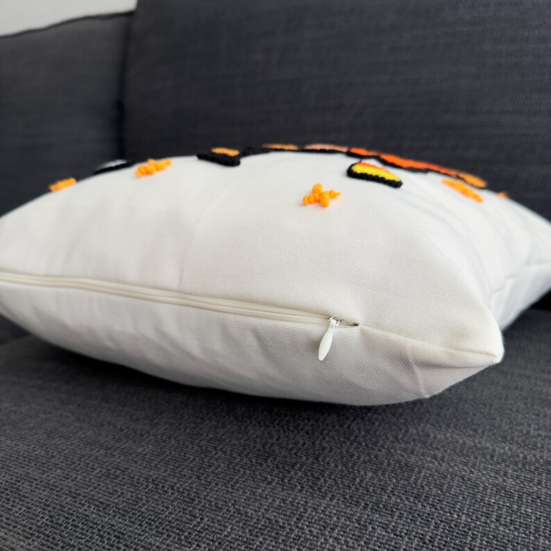 May include: White pillow with a zipper closure. The pillow has an orange and black embroidered design with small orange stars.