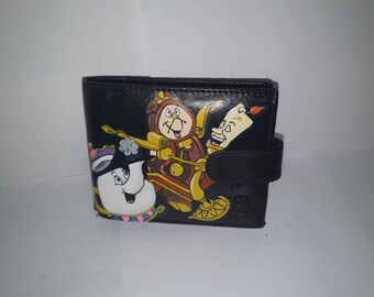 May include: Black leather wallet with a painted design featuring characters from the Disney film Beauty and the Beast. The characters include Lumiere, Cogsworth, and Mrs. Potts.