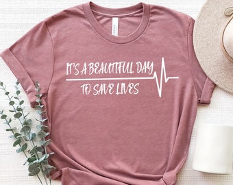 May include: A mauve t-shirt with a white graphic that reads "It's a beautiful day to save lives" with a heartbeat graphic.