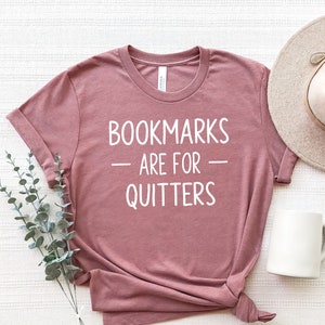 May include: A mauve t-shirt with the text "BOOKMARKS ARE FOR QUITTERS" printed in white.