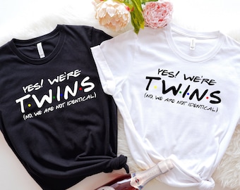 Może przedstawiać: Dwie czarno-białe koszulki z tekstem "YES! WE'RE TWINS (NO, WE ARE NOT IDENTICAL)" w stylizowanym kroju pisma. Tekst jest czarny z kolorowymi kropkami.