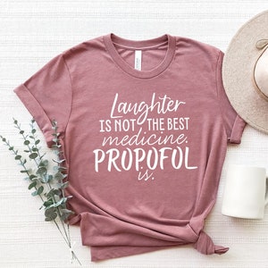 May include: A mauve t-shirt with the text "Laughter is not the best medicine. Propofol is." printed in white.