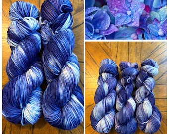 Puede incluir: Dos madejas de hilo teñido a mano con una paleta de colores variados en azul marino intenso, azul real y blanco, junto a una imagen más pequeña de flores de hortensia azules y moradas con gotas de agua en los pétalos.