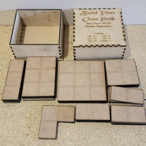 May include: Wooden box set for building your own path. The box contains various sized wooden tiles with a black border. The box lid has the text "Build Your Own Path" and "Basic Terrain Tile Set" with a list of tile sizes and quantities.