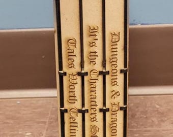 May include: A wooden Dungeons & Dragons dice tower with engraved text. The tower is rectangular with black accents and features the D&D logo. The text includes "Dungeons & Dragons", "It's the Character's Story", and "Tales Worth Telling".