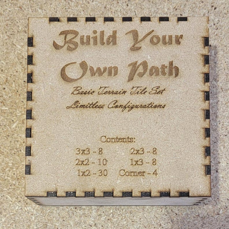 May include: Wooden box with the text "Build Your Own Path" and "Basic Terrain Tile Set" on the top. The box contains a set of wooden tiles for a game or craft project. The contents are listed as: 3x3 - 8, 2x3 - 8, 2x2 - 10, 1x3 - 8, 1x2 - 30, Corner - 4.