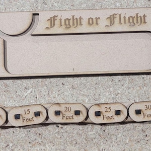 Puede incluir: Un accesorio de juego de madera Fight or Flight. El conjunto incluye una pieza rectangular con el texto "Fight or Flight" y una ranura curva, y una regla segmentada marcada de 1,5 a 12,2 metros.