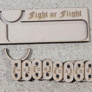 Puede incluir: Accesorio de juego de madera cortado con l&aacute;ser con el texto "Fight or Flight". Incluye una bandeja y marcadores de distancia de 1,5 a 12,2 metros. El accesorio est&aacute; hecho de madera clara.