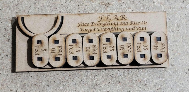 Puede incluir: Placa de madera con la inscripci&oacute;n F.E.A.R. (Face Everything and Rise Or Forget Everything and Run) y ocho marcadores de distancia extra&iacute;bles, de 1,5 a 12 metros. La placa tiene una parte superior curvada y es de madera clara.