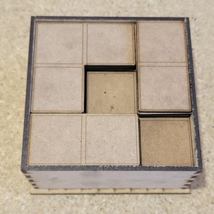 May include: A wooden box with nine square compartments, each with a light brown surface. The box is made of dark wood and has a black border around each compartment.