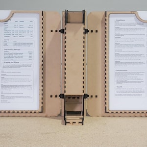 Könnte beinhalten: Ein hölzerner Tischspielbildschirm mit vier Paneelen, die jeweils ein weißes Blatt Papier mit gedrucktem Text enthalten. Die Paneele sind durch Scharniere verbunden und haben einen dekorativen Rand. Der Bildschirm ist so konzipiert, dass er aufrecht steht.